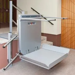 Platforma przyschodowa dla osób z niepełnosprawnościami, model Flex 3, zamontowana przy schodach z beżowymi ścianami i drewnianymi drzwiami.