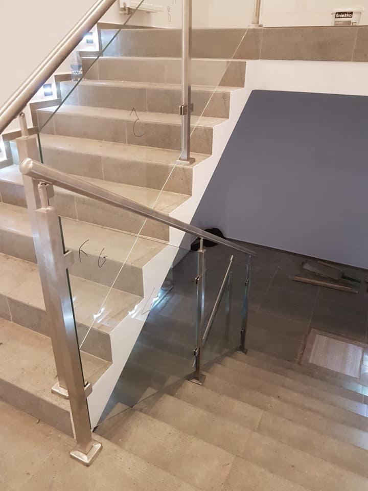 Schody wykończone szarym kamieniem z nowoczesną szklaną balustradą i stalowymi poręczami, widoczne ślady po ołówku na stopniach, oraz puszka farby w tle.