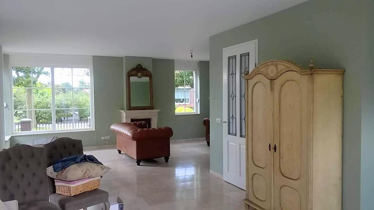 Salon po odświeżeniu z zielonymi ścianami, kremową szafą w stylu vintage, skórzaną sofą i marmurową podłogą.