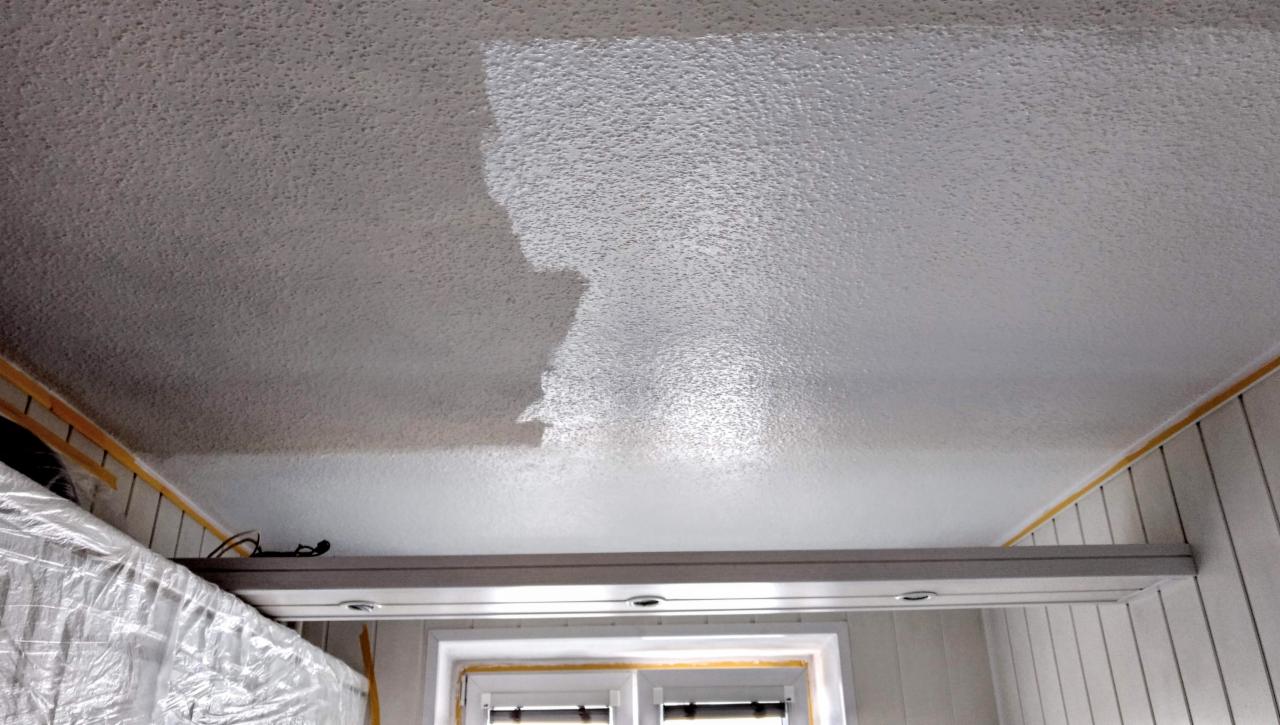 Fragment pomalowanego sufitu z fakturą baranka, widoczne niedomalowane obszary i taśma malarska przy ścianie, okno w tle.