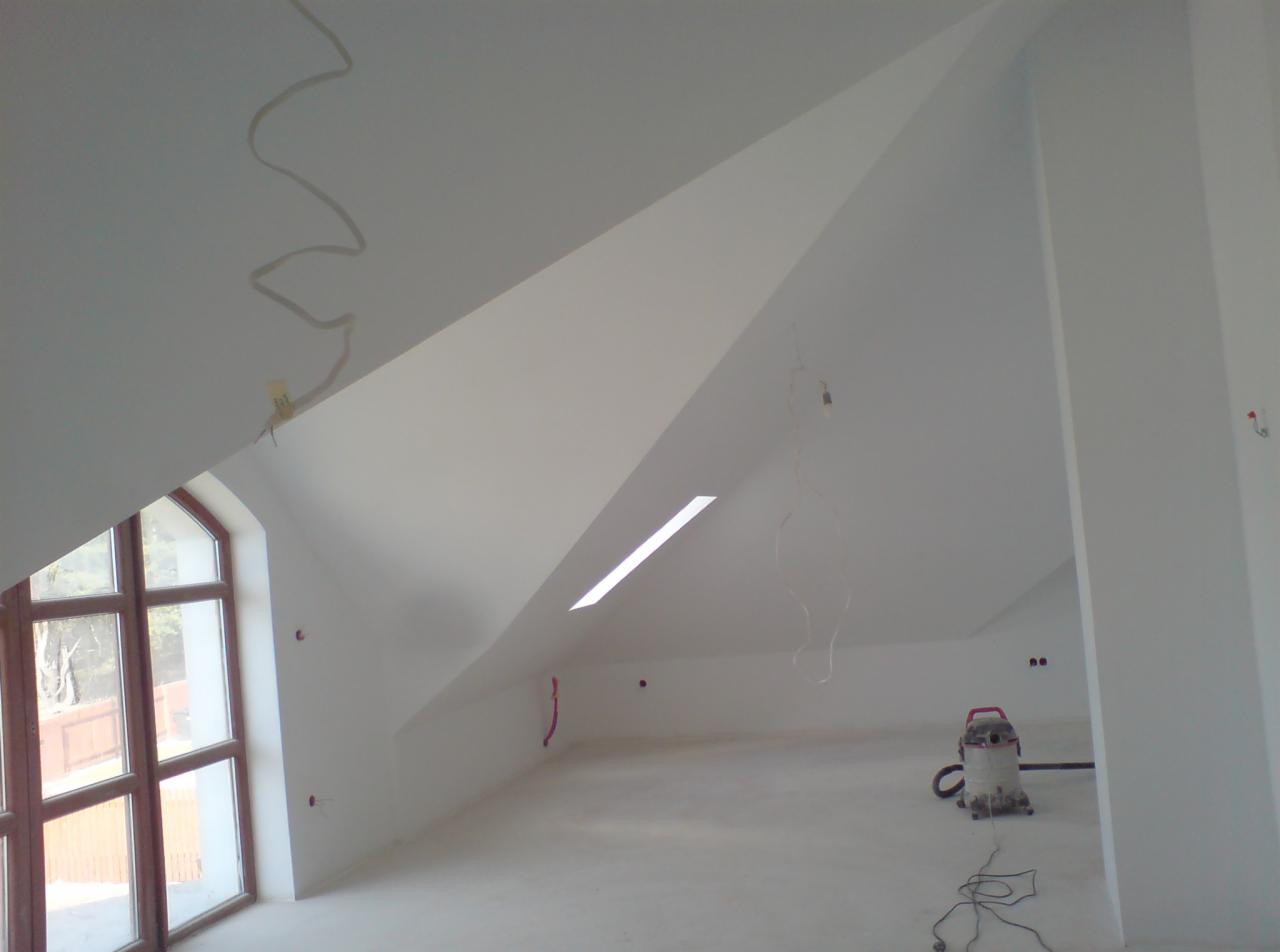Poddasze po remoncie, świeżo pomalowane na biało, z widocznym oknem dachowym i odkurzaczem przemysłowym, wystające przewody elektryczne.