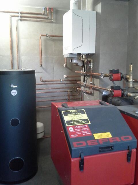 Zainstalowany piec gazowy z widocznymi rurami miedzianymi i zbiornikiem buforowym w kotłowni w Skawinie. Widoczny również zasobnik na paliwo stałe z naklejką informacyjną.