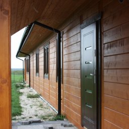 RIWKE - Zewnętrzny widok brązowego domu z drewnianą elewacją, ciemnymi oknami i drzwiami, oraz czarnymi rynnami.