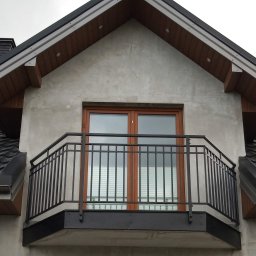 Z.P. KONSTAL - Czarna, metalowa balustrada balkonowa z prostymi szczeblami, zamontowana przed dwuskrzydłowymi drzwiami balkonowymi w domu z szarą elewacją i ciemną dachówką.