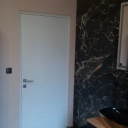 Nowoczesna łazienka z czarną ścianą imitującą marmur, drewnianą podłogą i trzema okrągłymi lampami z drewnianymi elementami.