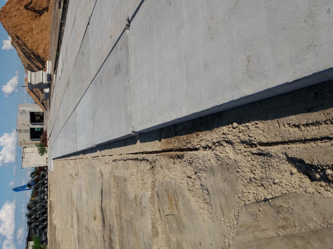 Betonowe płyty ułożone na ziemi w miejscowości Skopanie, widoczne ślady po wykopie i przygotowaniu terenu, w tle składowane materiały budowlane.