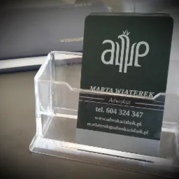 Wizytówka adwokat Marty Wiaterek w przezroczystym plastikowym stojaku na biurku, widoczny numer telefonu i adres strony internetowej.