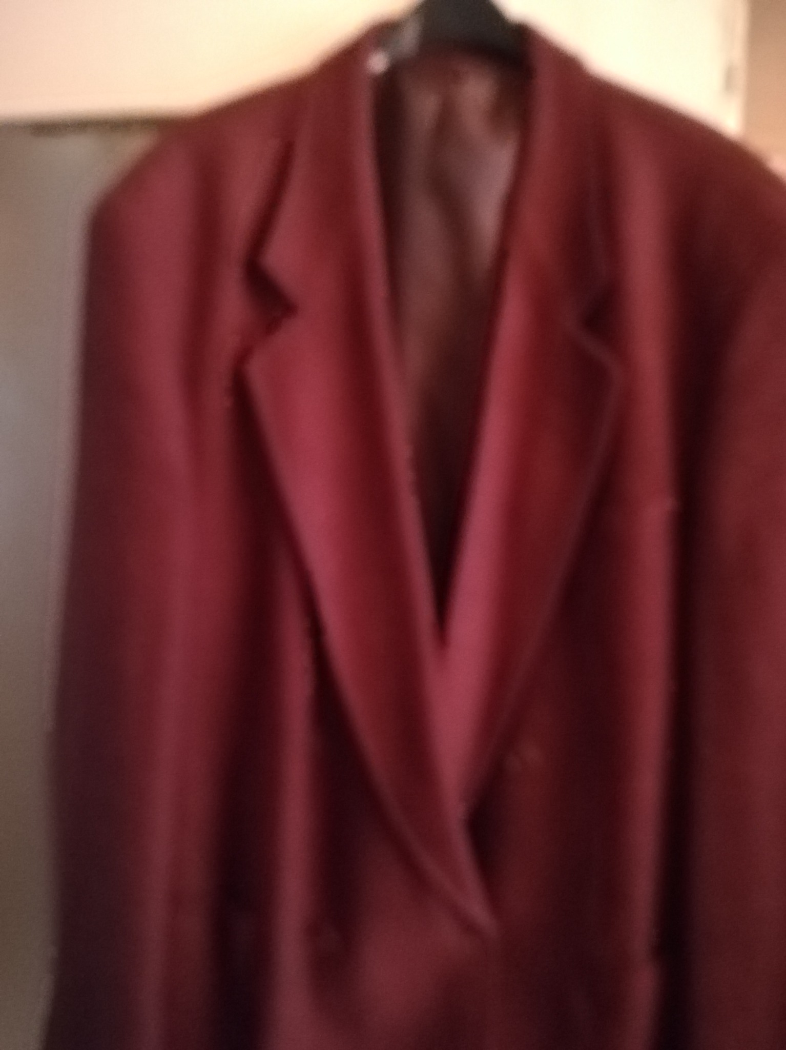 Rozmazane zdjęcie używanego, bordowego, dwurzędowego płaszcza męskiego wiszącego na wieszaku.