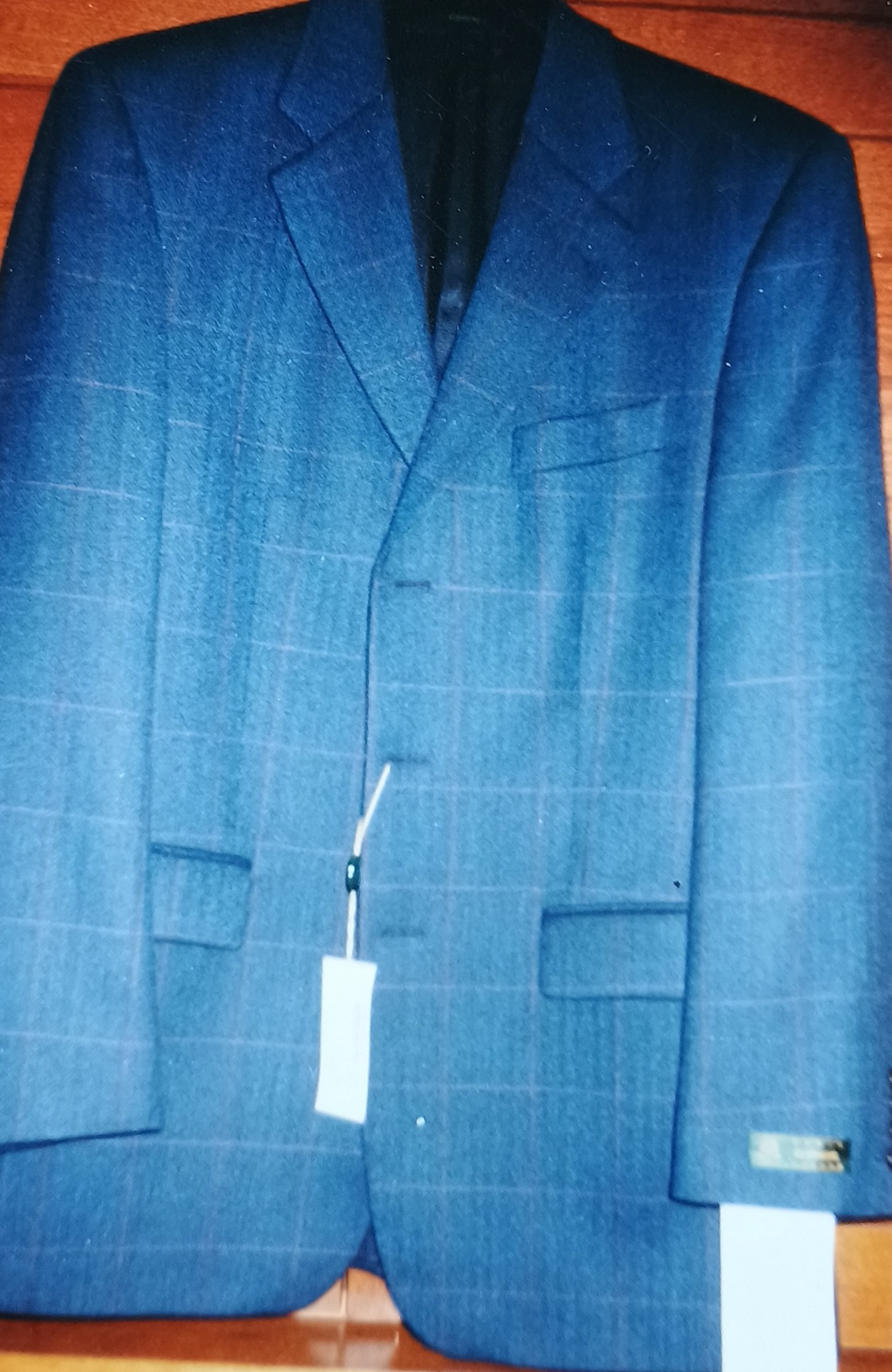 Niebieska marynarka w kratę z metką, wisząca na drewnianym tle.