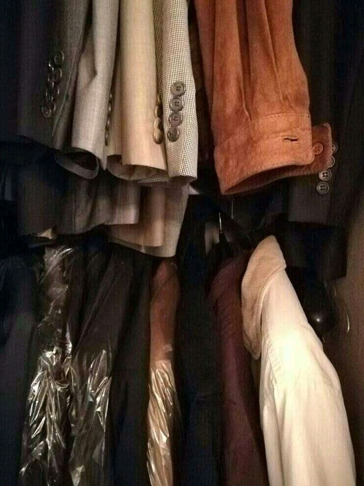 Rząd wiszących marynarek i koszul w szafie, niektóre z nich w plastikowych pokrowcach, w odcieniach brązu, beżu i czerni.