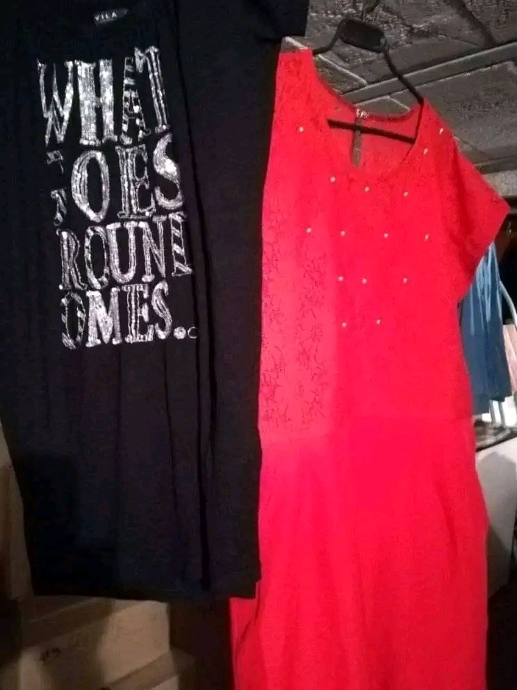 Czerwona sukienka z krótkim rękawem i czarny T-shirt z napisem na wieszaku, słabe oświetlenie.