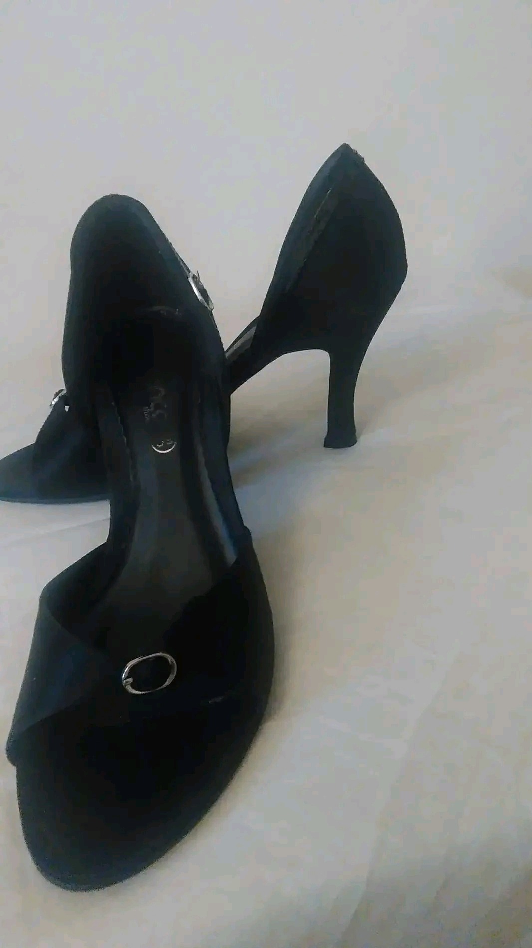 Para czarnych zamszowych butów do tańca z odkrytymi palcami i srebrnymi sprzączkami, ustawiona na jasnym tle.