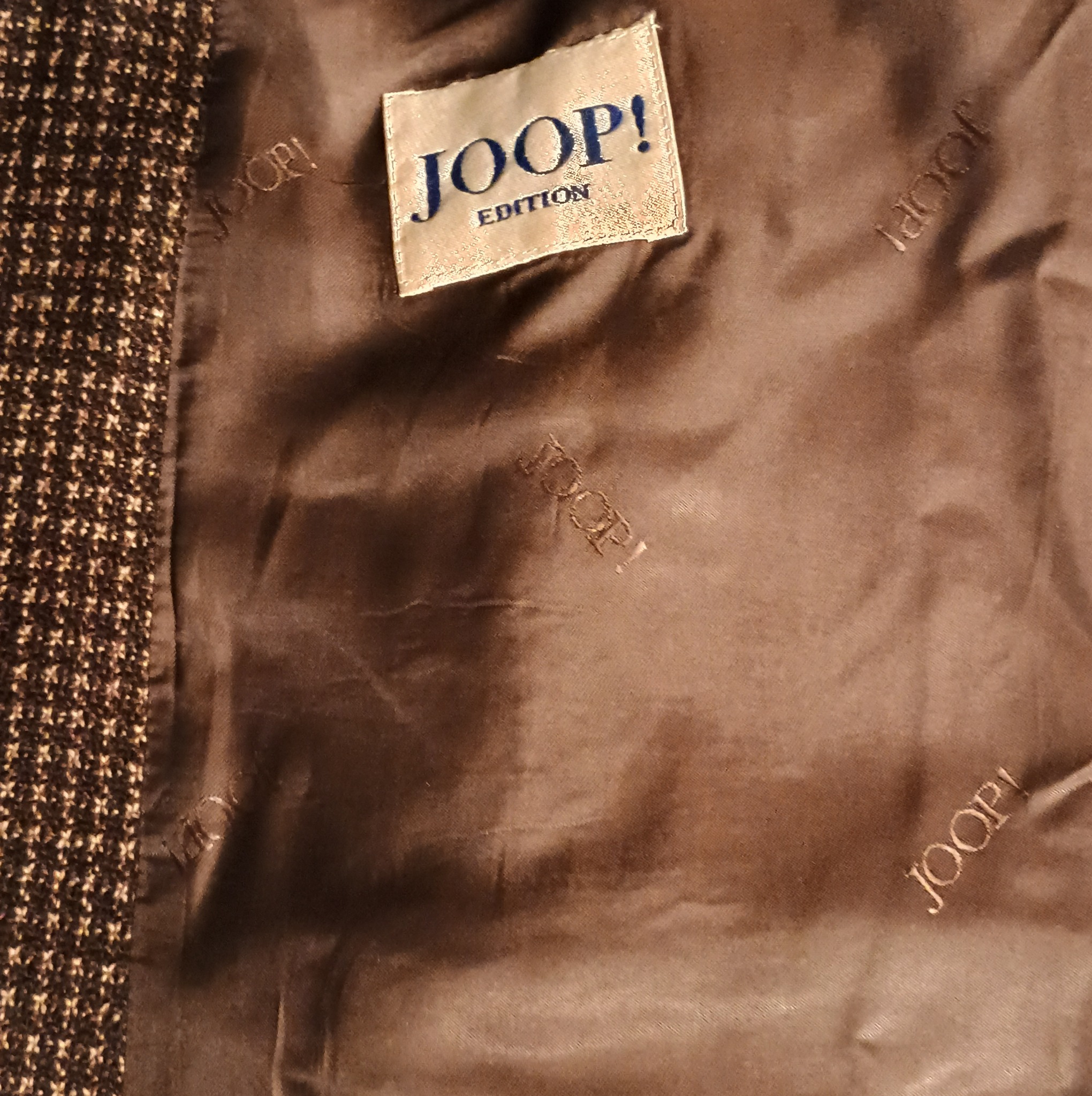 Wnętrze brązowej marynarki z widoczną metką marki JOOP! Edition i powtarzającym się, subtelnym haftem z nazwą marki na podszewce.
