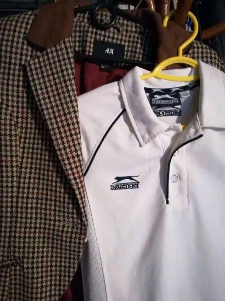 Marynarka w brązową kratę obok białej koszulki polo marki Slazenger na żółtym wieszaku.