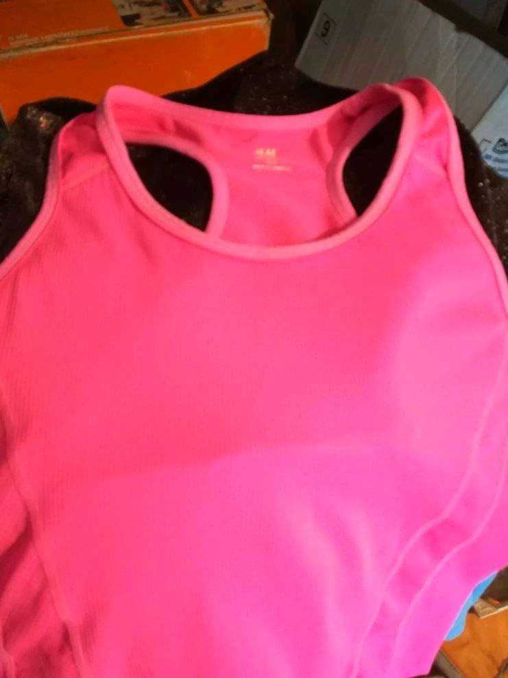 Jasnoróżowy sportowy top z widocznym logo marki H&M, leżący na ciemnym tle.