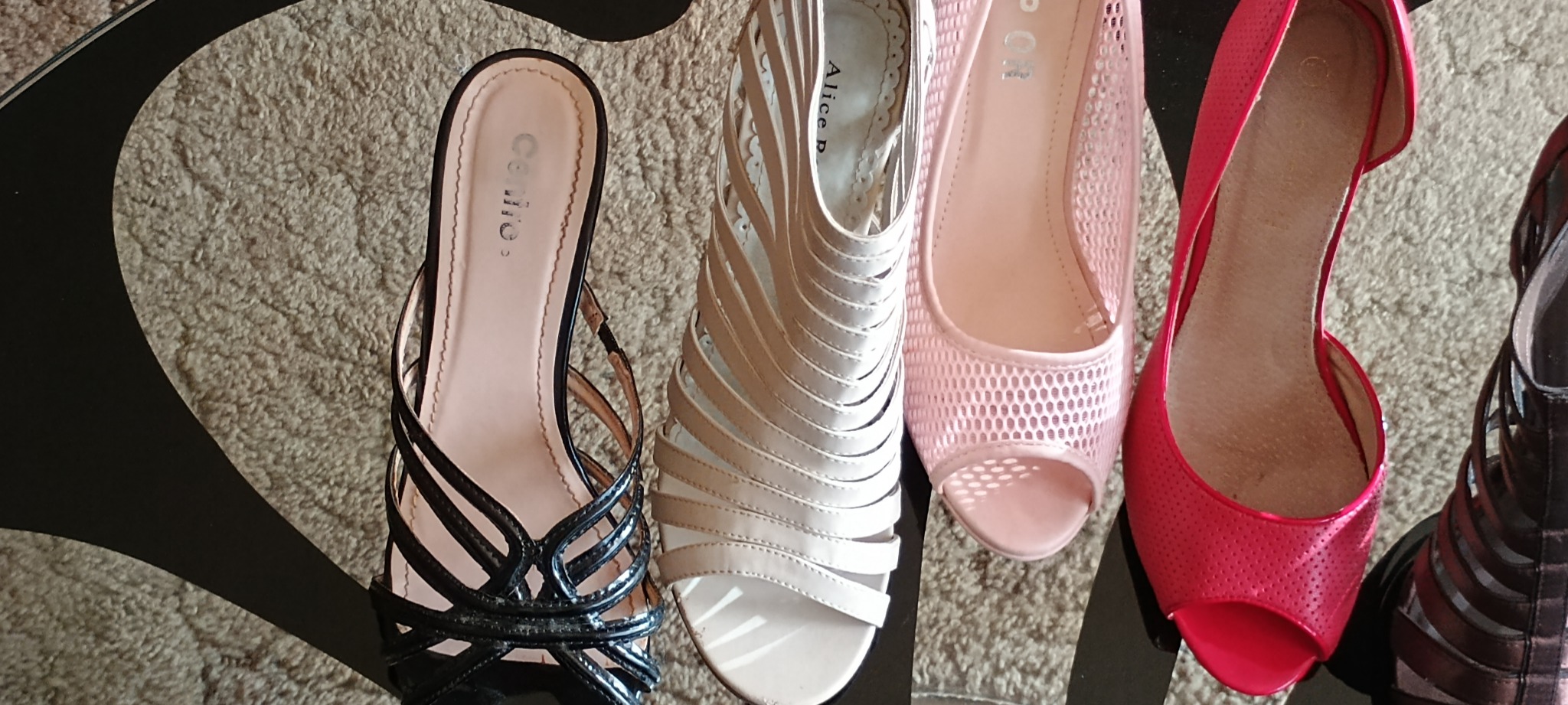 Kolekcja czterech par używanych damskich butów na obcasie: czarne sandały z paskami, beżowe sandały z wycięciami, różowe ażurowe czółenka i czerwone czółenka z wycięciem, leżące na dywanie.