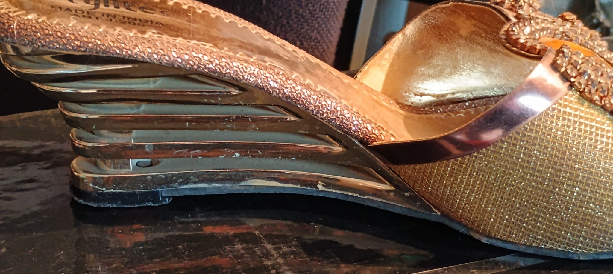 Złoty damski but na koturnie z ozdobnymi kamieniami, widoczna podeszwa i konstrukcja koturna z poziomymi przerwami.