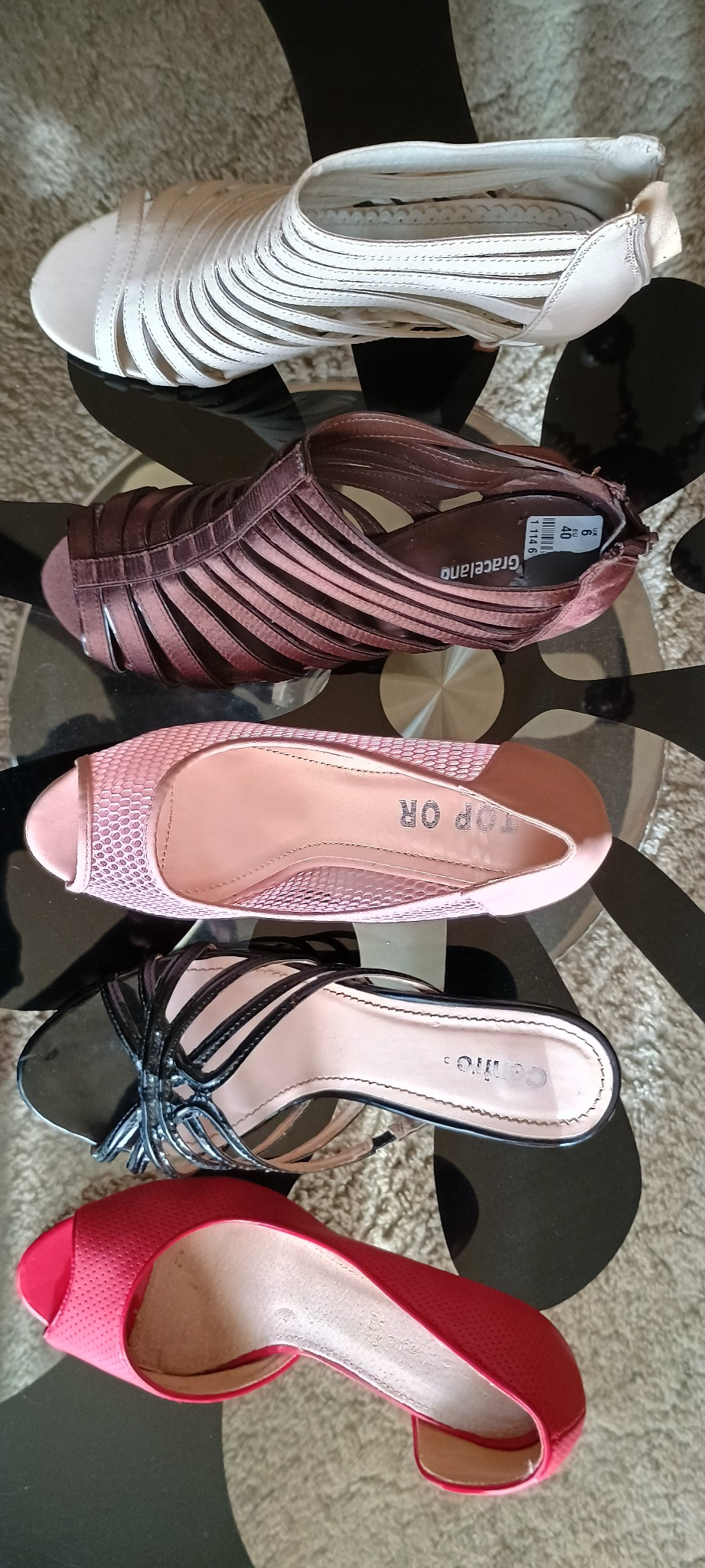 Kolekcja pięciu par damskich butów na obcasie, w różnych kolorach i fasonach, ułożonych jeden na drugim na wzorzystym stole.