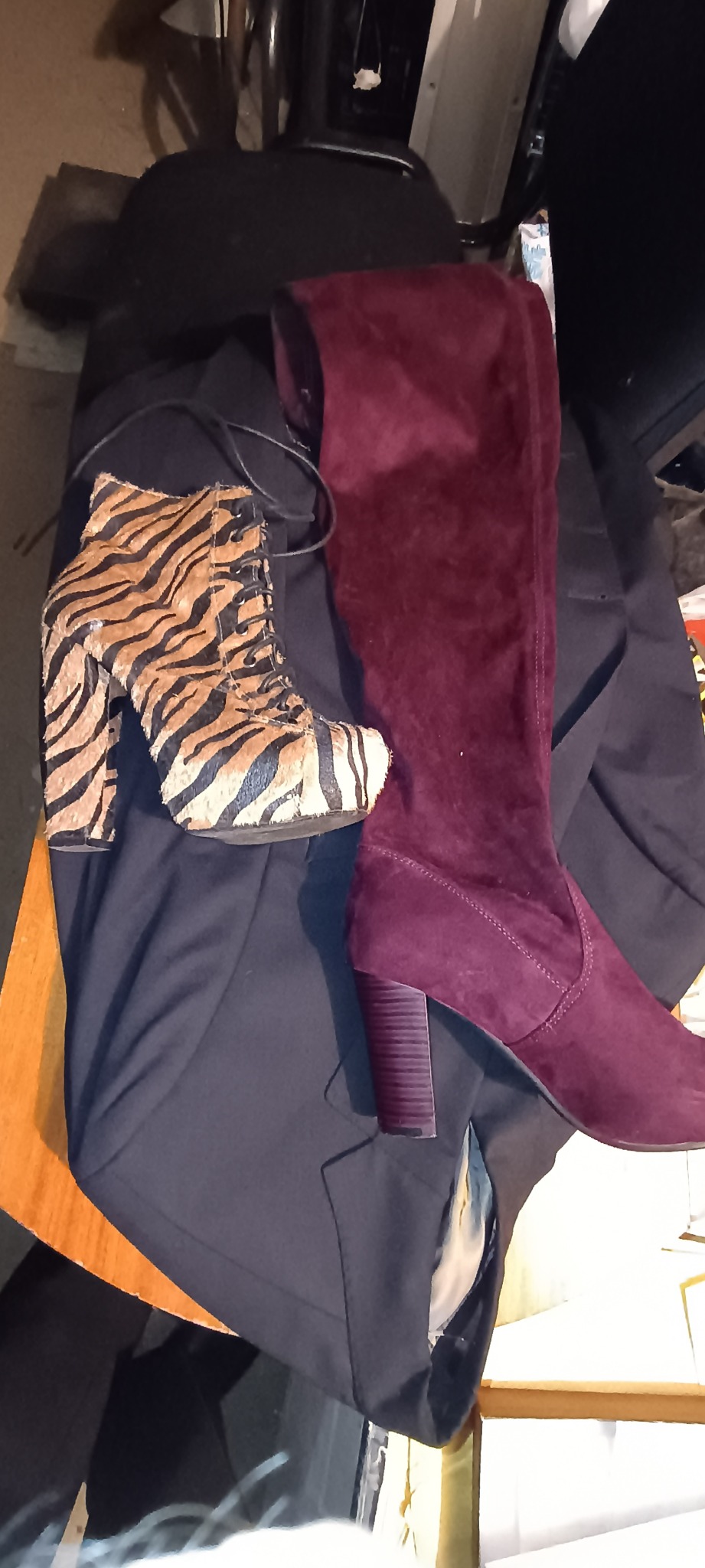 Para butów: botki sznurowane w zwierzęcy wzór zebry i bordowe kozaki za kolano z zamszu, leżące na ciemnym ubraniu.