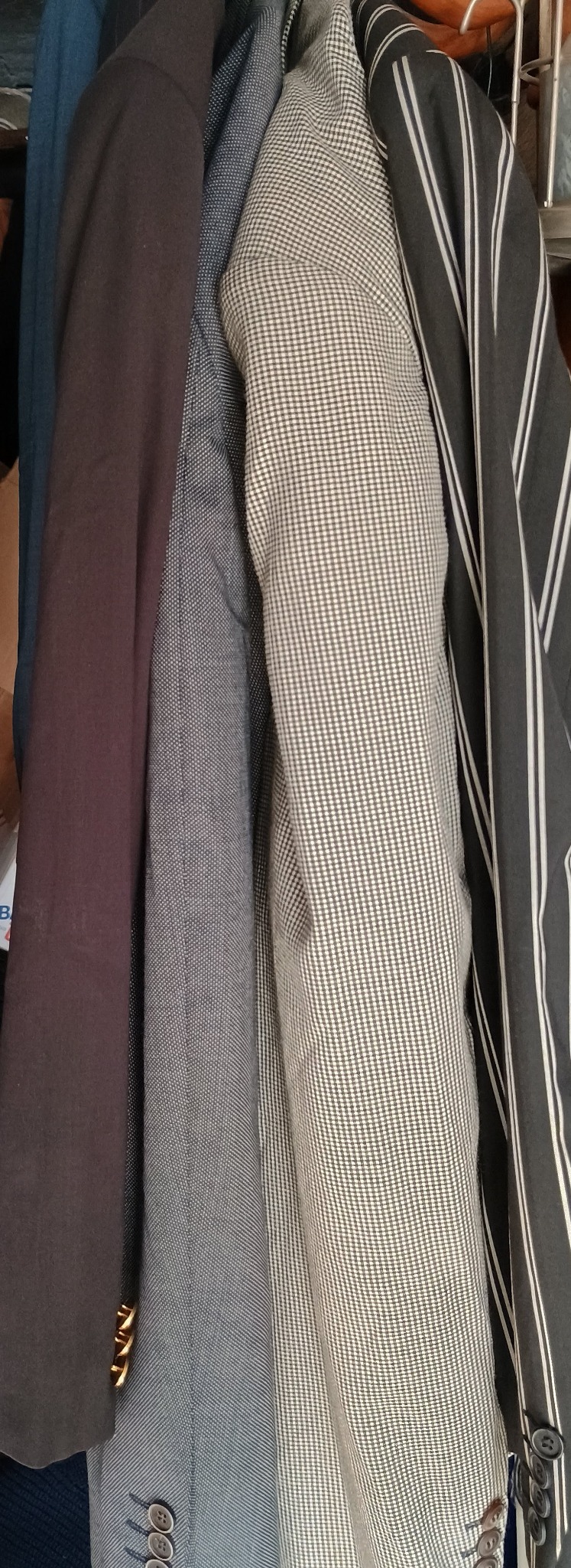 Używane marynarki wiszące obok siebie: brązowa, niebieska w drobną kratkę, beżowa w kratkę gingham i szara w białe paski.