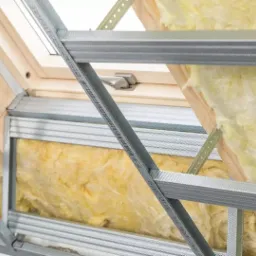 Ocieplenie poddasza wełną mineralną widoczne przez metalowy stelaż pod płyty karton-gips, okno dachowe w tle.