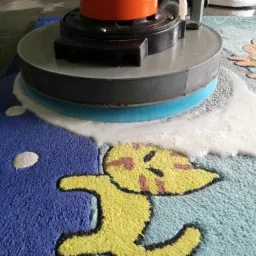 Automat do czyszczenia dywanów w trakcie pracy na dywanie dziecięcym z wzorami zwierząt, z widoczną pianą czyszczącą.