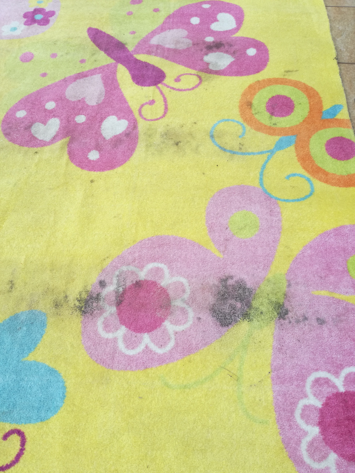 Żółty dywan dziecięcy z wzorami motyli i kwiatów, widoczne zabrudzenia i plamy.