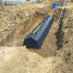 Instalacja podziemnego zbiornika retencyjnego w wykopie, z widoczną poziomicą na g&oacute;rze konstrukcji i warstwą żwiru wok&oacute;ł