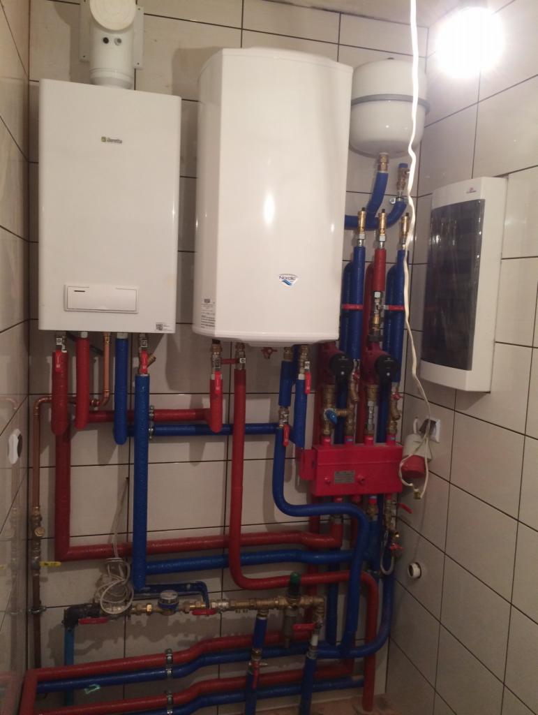 Białe kotły gazowe Beretta i Nordic z czerwono-niebieską instalacją rurową na tle kafelkowanej ściany.