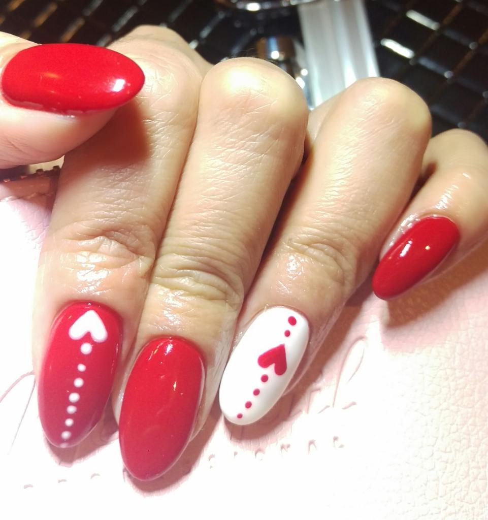 Dłoń z czerwonymi i białymi paznokciami w kształcie migdała, ozdobionymi motywem serca i kropek