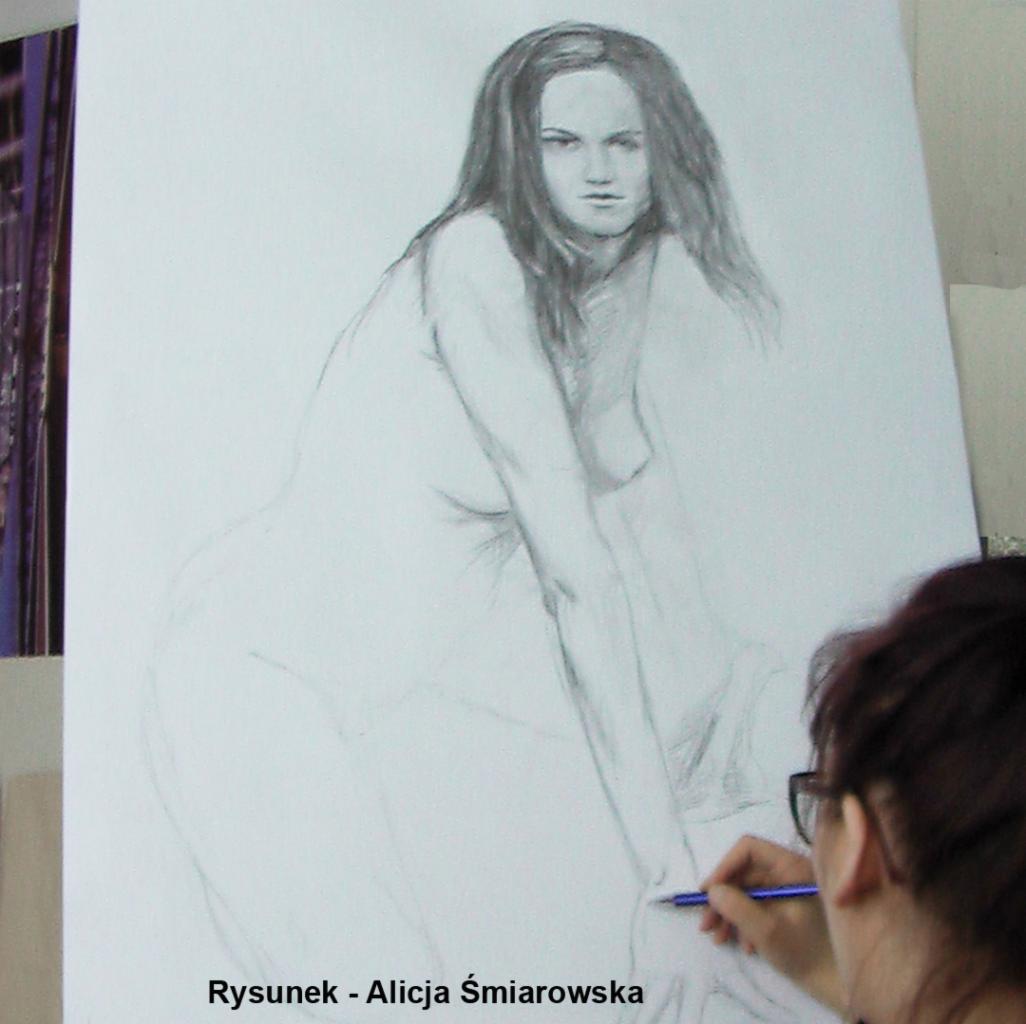 Rysunek ołówkiem przedstawiający akt kobiety, w trakcie tworzenia, z widoczną ręką artysty trzymającą ołówek.