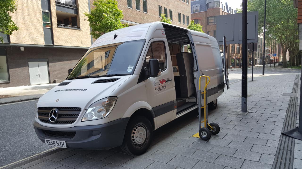 Biały Mercedes Sprinter z otwartymi drzwiami bocznymi, zaparkowany na chodniku, z wózkiem transportowym obok, widoczny adres strony internetowej i numer telefonu firmy na boku pojazdu.