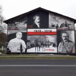 Duży mural na ścianie budynku upamiętniający 100-lecie odzyskania niepodległości przez Polskę, z portretami postaci historycznych, scenami batalistycznymi i datą 1918-2018.