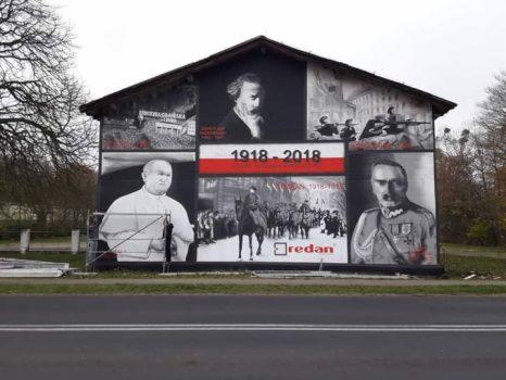 Duży mural na ścianie budynku upamiętniający 100-lecie odzyskania niepodległości przez Polskę, z portretami postaci historycznych, scenami batalistycznymi i datą 1918-2018.