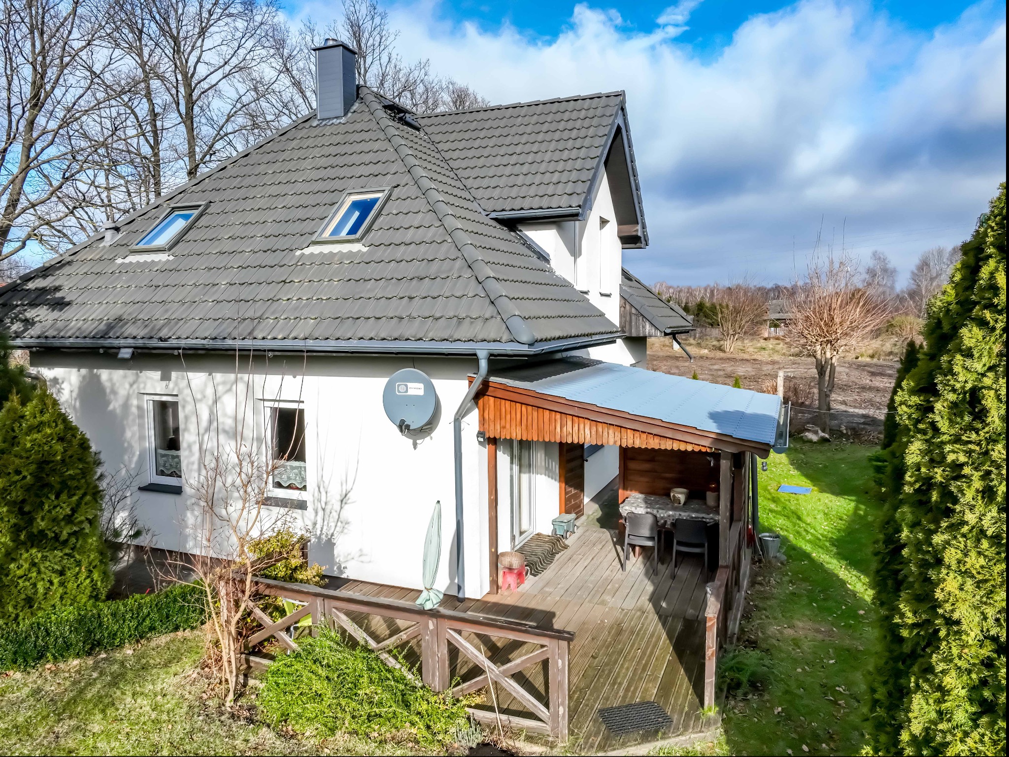 Dom jednorodzinny z szarą dachówką i drewnianym tarasem, widok z góry. Antena satelitarna na elewacji. Kopalino.