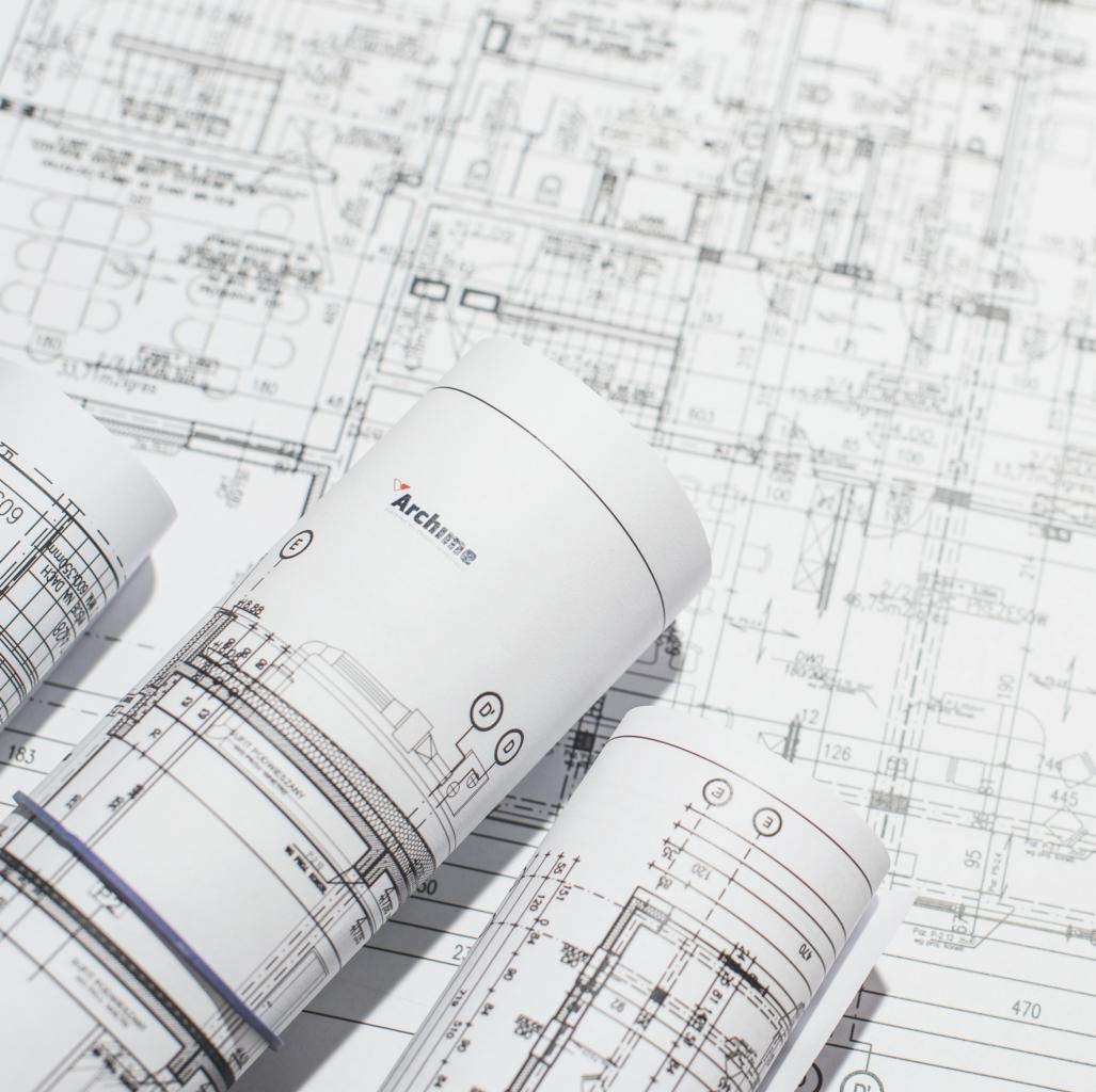 Zrolowane plany architektoniczne z logo firmy Archime na tle rozłożonego rysunku technicznego.