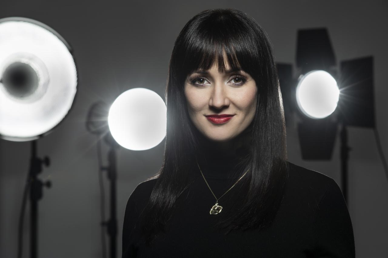 Portret kobiety w czarnym golfie, z ciemnymi włosami i czerwonymi ustami, pozującej w studio oświetlonym lampami błyskowymi.