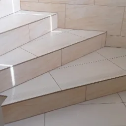 Schody wyłożone beżowymi płytkami imitującymi marmur, z metalową poręczą, widoczne z dołu pod kątem.