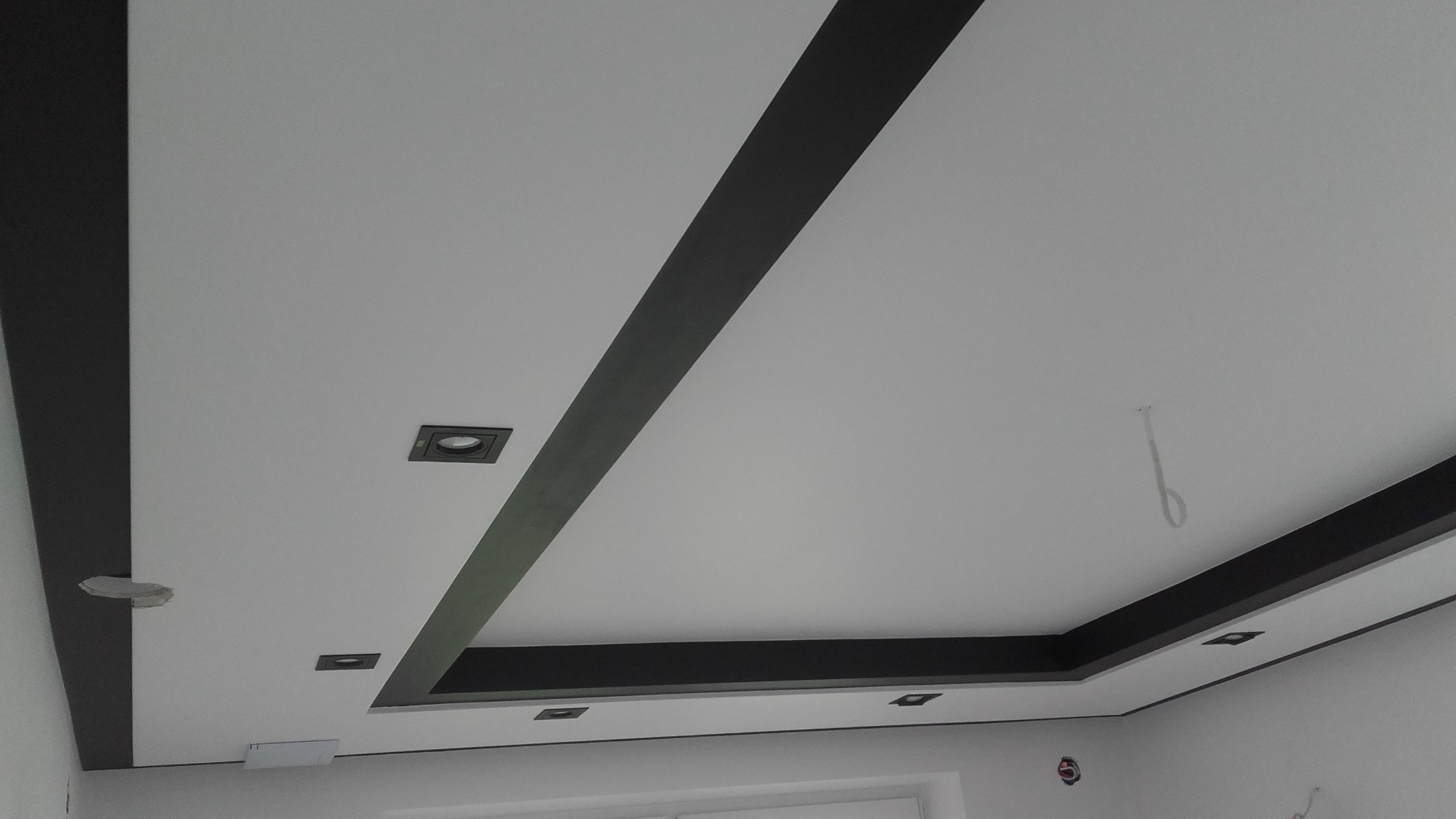 Biały sufit z czarnymi, geometrycznymi elementami dekoracyjnymi i wbudowanymi punktami świetlnymi.
