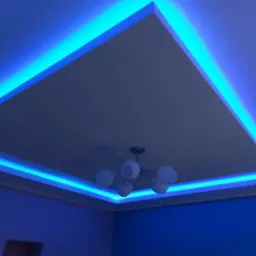 Podwieszany sufit z oświetleniem LED w kolorze niebieskim, widoczny z perspektywy narożnika pokoju, z żyrandolem z mlecznymi kulami w centralnej części.