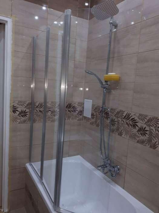Wykończona łazienka z wanną, szklanym parawanem nawannowym i nowoczesną armaturą prysznicową na tle beżowych płytek z motywem liści.