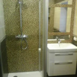 Ukończona łazienka z kabiną prysznicową, umywalką z szafką i mozaiką na ścianie, z nietypowym ułożeniem lustra.