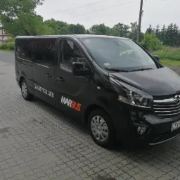 Czarny bus Opel Vivaro z logo Marbus i numerem telefonu zaparkowany na kostce brukowej przed budynkiem.