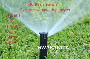 Zraszacz trawnikowy podczas pracy, rozpylający wodę. Widoczne napisy z nazwami firm i informacją o gwarancji, sugerujące montaż i serwis systemów nawadniających.