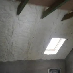 Poddasze ocieplone pianką PUR z widocznym oknem dachowym i drewnianą konstrukcją dachu, surowy stan ścian poniżej ocieplenia.