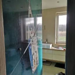 Wnętrze łazienki z szafą wnękową z fototapetą przedstawiającą żaglówkę, widok na umywalkę, blat i okno z widokiem na zewnątrz.