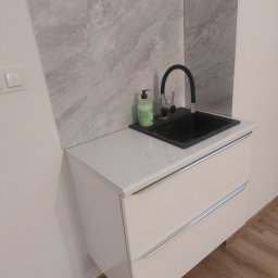 Sławomir Pożarowski - Nowoczesna łazienka: czarna umywalka z baterią na białej szafce z szufladami, marmurowe płytki na ścianie. Minimalistyczny design, butelka mydła w tle.