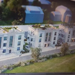 Wizualizacja osiedla nowoczesnych, trzypiętrowych budynków z tarasami na dachach i balkonami, otoczonych zielenią.