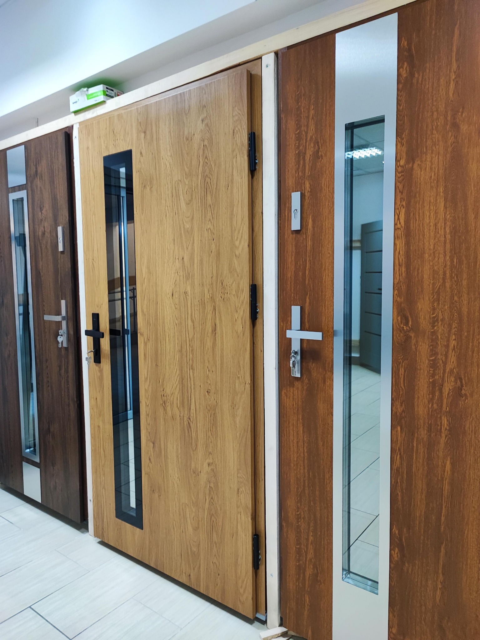 Wystawa trzech modeli drzwi wewnętrznych z różnymi wykończeniami i przeszkleniami, prezentowanych w salonie sprzedaży.