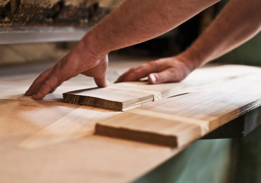 Ręce stolarza dopasowujące elementy drewniane na blacie podczas montażu, widoczne niedoskonałości krawędzi.
